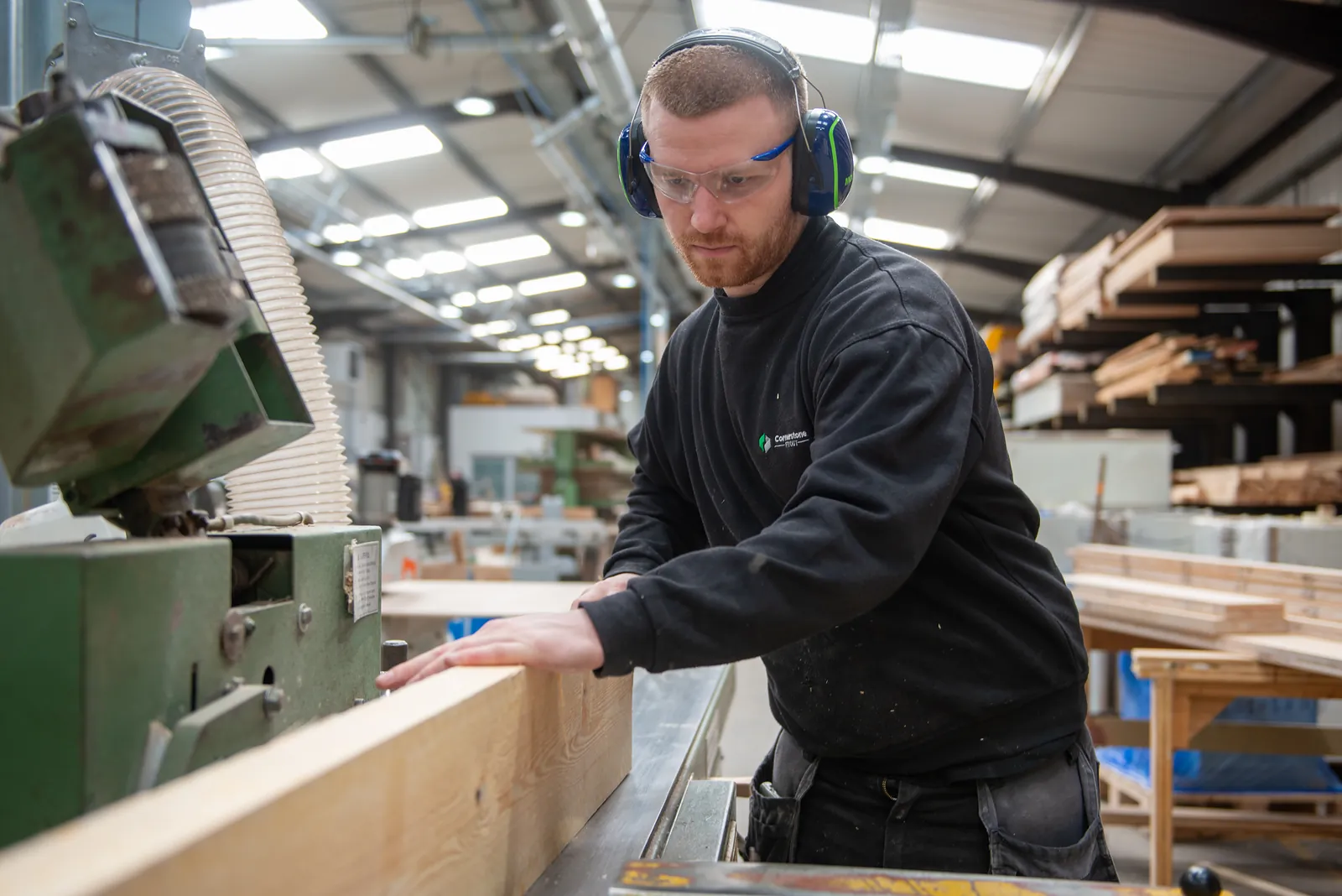 Joiner in safety glasses and ear defenders machining timber in the Cornerstone workshop
