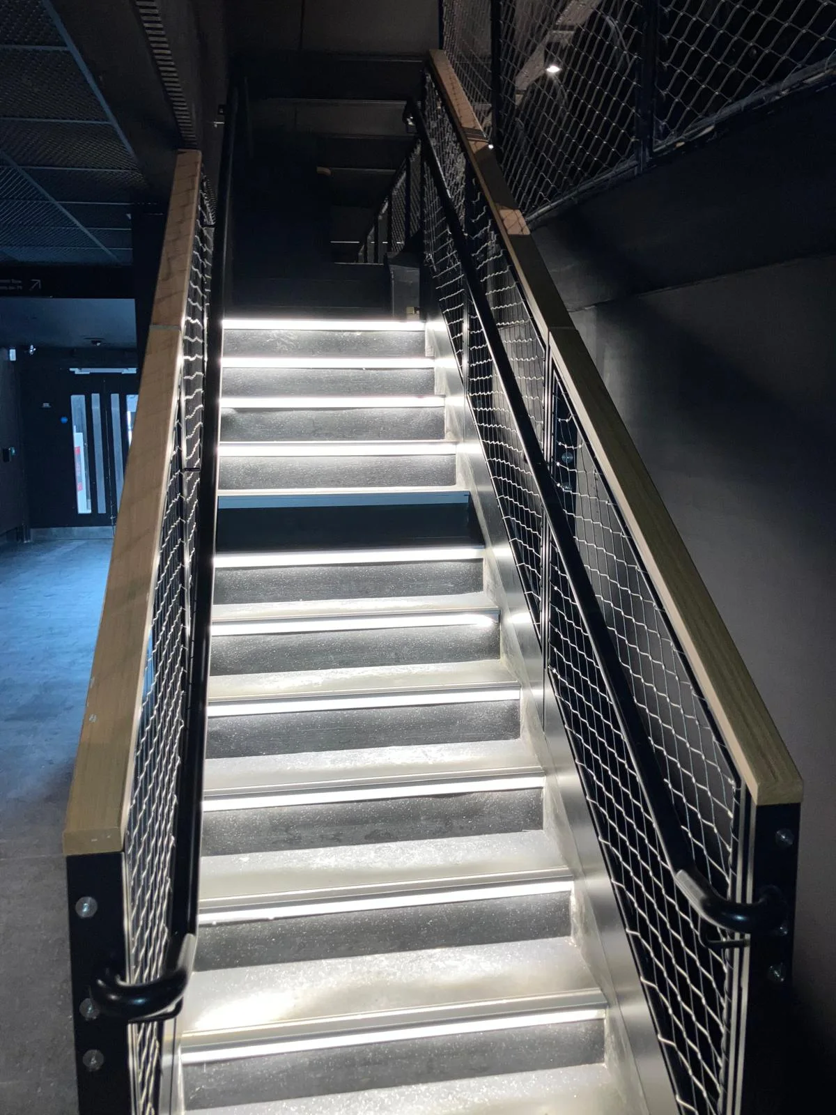 Black steel stair with woven mesh balustrade infill, oak handrail capping and LED-lit treads