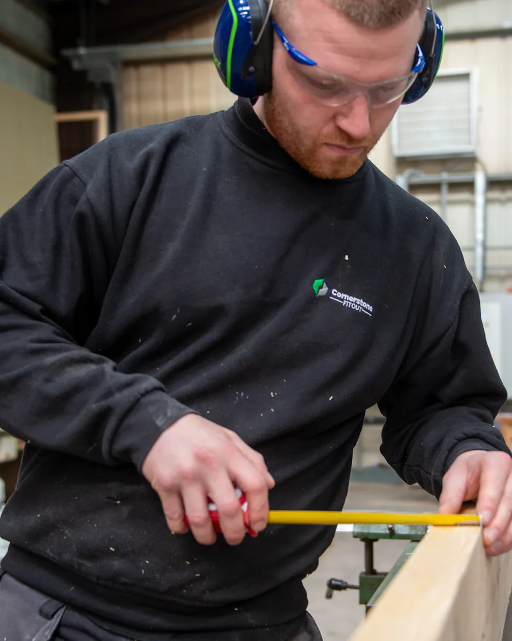 A Cornerstone joiner in safety glasses and ear defenders measuring timber in our Lancashire workshop