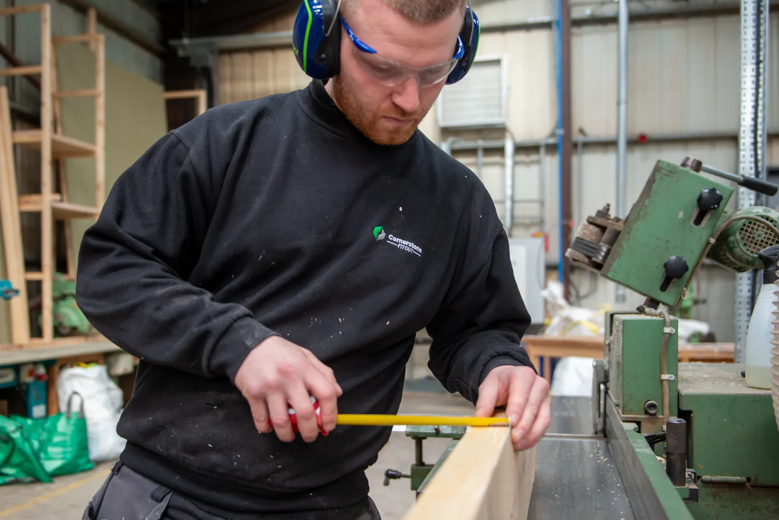 Joiner measuring timber, glasses and ear defenders on