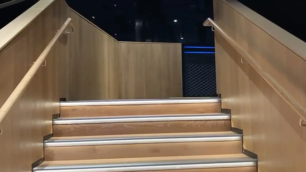 Foot of an oak-clad staircase with LED-lit nosings and oak handrails on brushed brackets